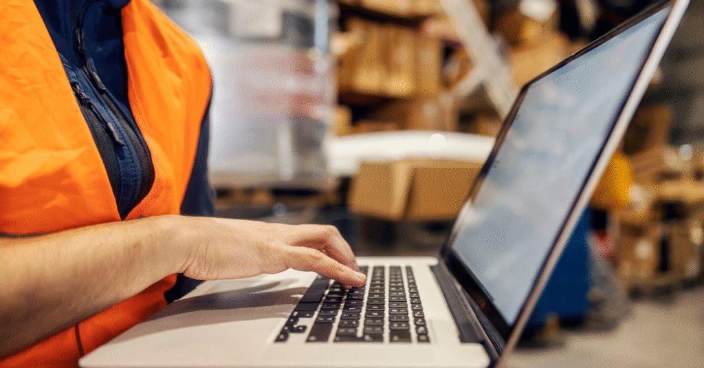 Cropped picture of stock clerk typing on laptop at warehouse and tracking shipment online.