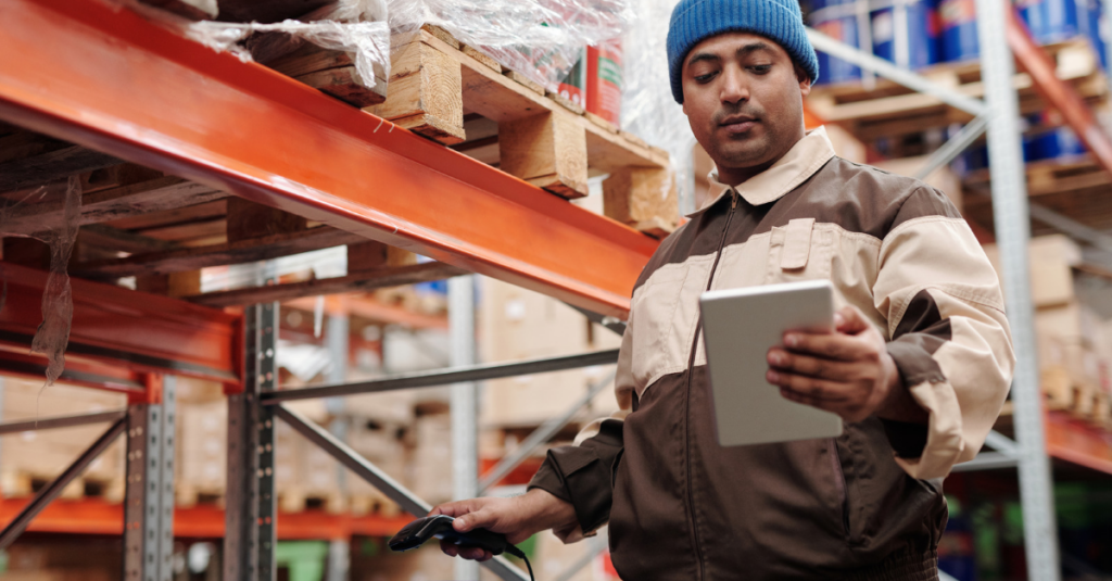 Person using tablet and barcode scanner to verify inventory on warehouse storage rack.